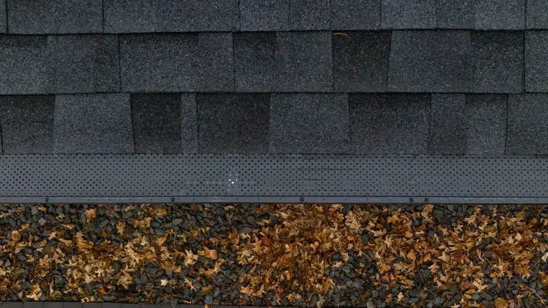 Seamless gutter with guard along a shingle roof edge